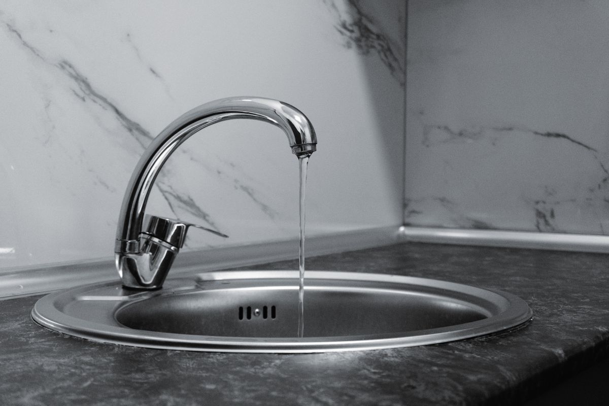 Chrome kitchen faucet running water over a stainless sink