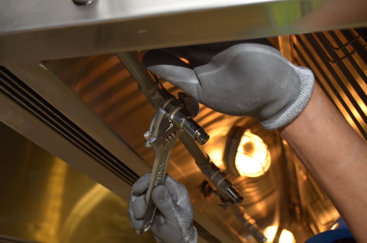 Gloved hand using a wrench on a fitting under a sink