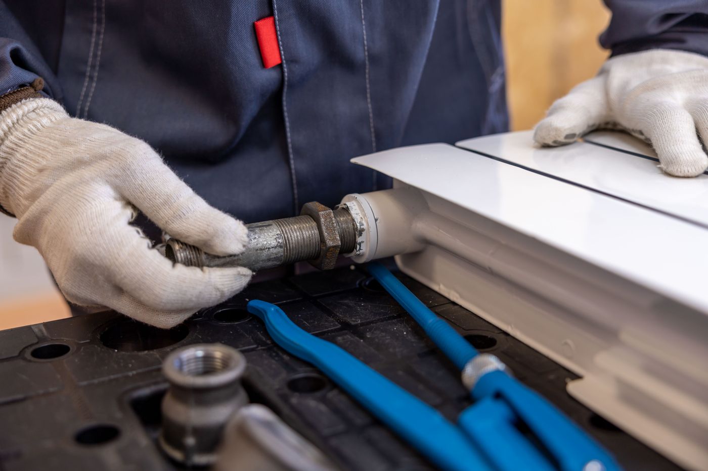 Gloved hands working on a length of pipe at a bench